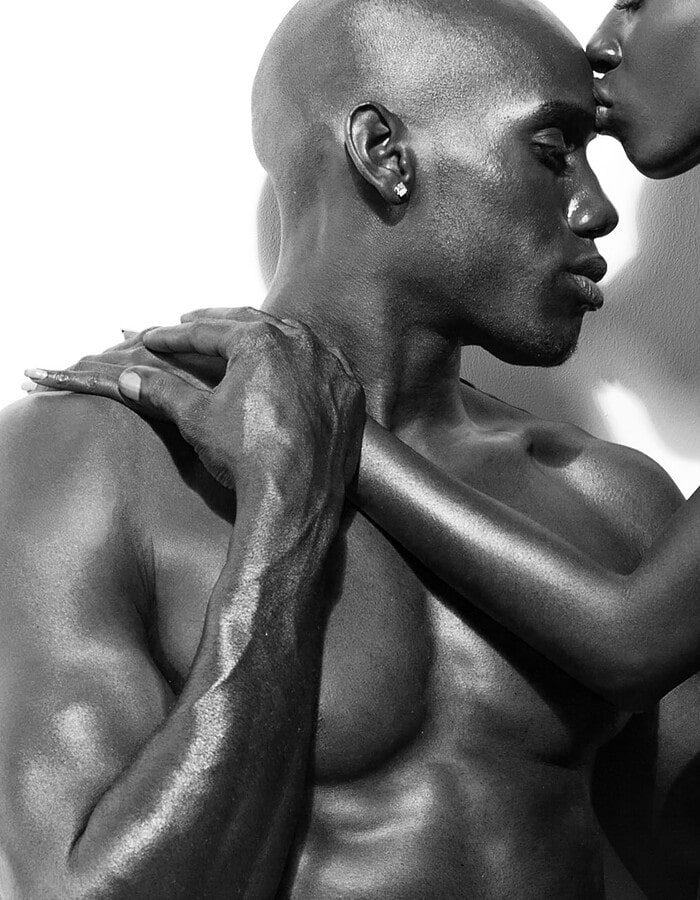 Closely cropped black-and-white portrait of two models holding one another.