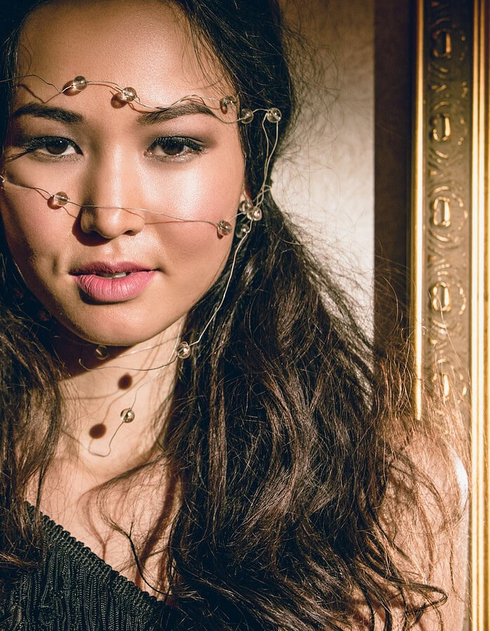 Close beauty portrait of a fashion model wearing delicate wire face jewelry beside an ornate mirror.