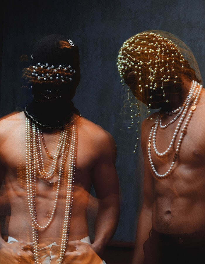 Two models in pearl-decorated masks photographed with layered motion blur against a dark blue background.