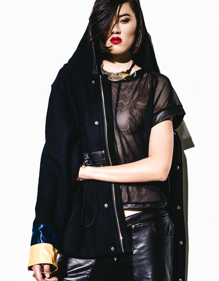 Fashion model wearing a black mesh top, leather-panel trousers and an oversized dark coat.