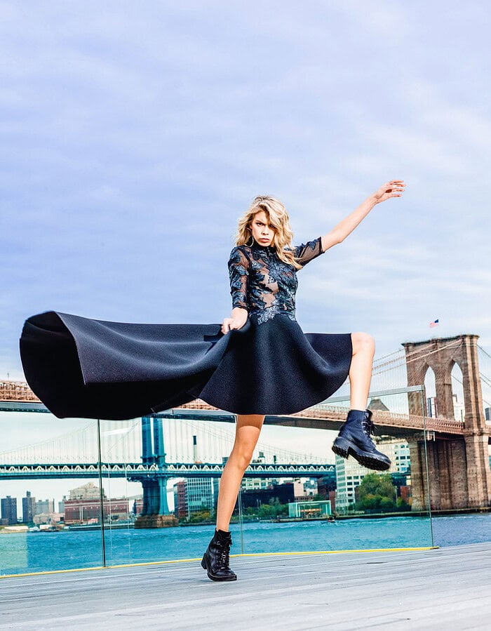 Fashion model lifting a sculptural black skirt on the waterfront with the Brooklyn Bridge in the background.