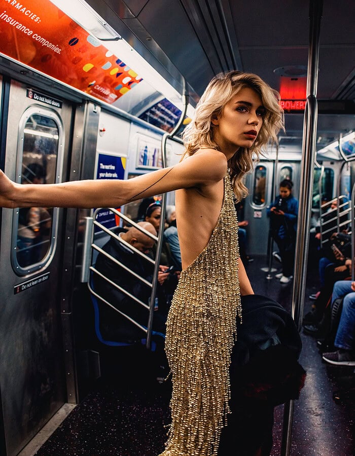 Fashion model holding a subway pole while wearing a backless sparkling gold outfit.