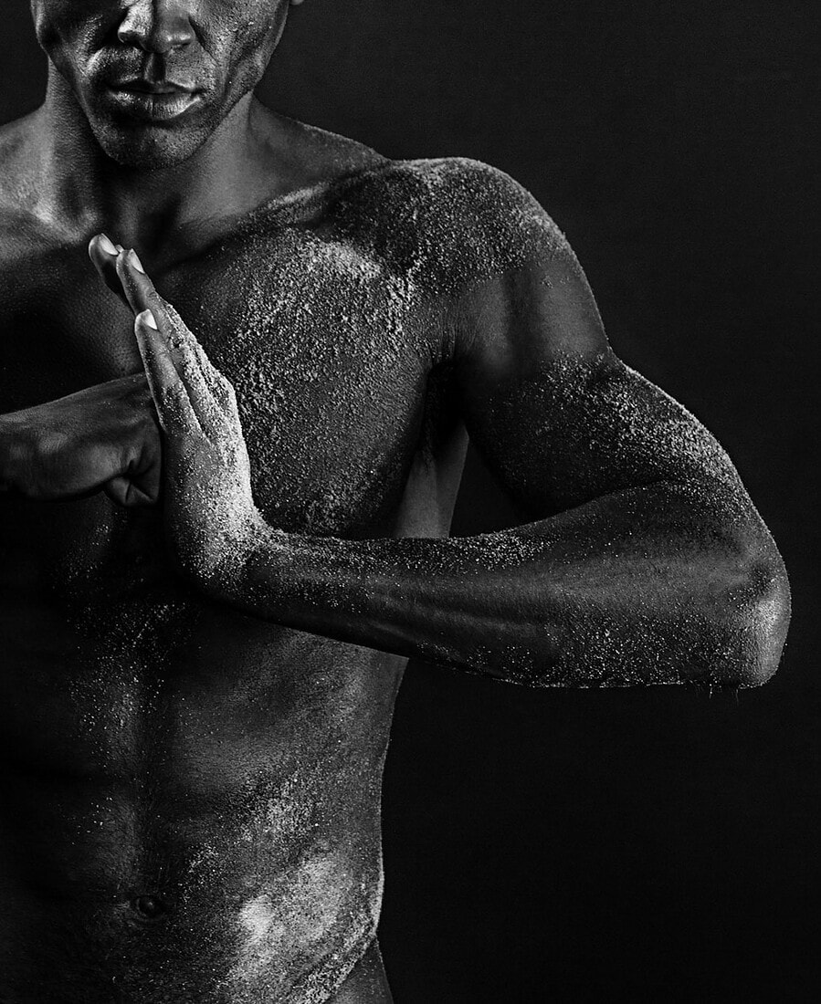 Study Cropped black-and-white portrait of a male model pressing his hands together across a sand-textured torso.