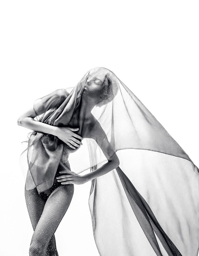 Dancer leaning sideways as translucent fabric extends through the frame