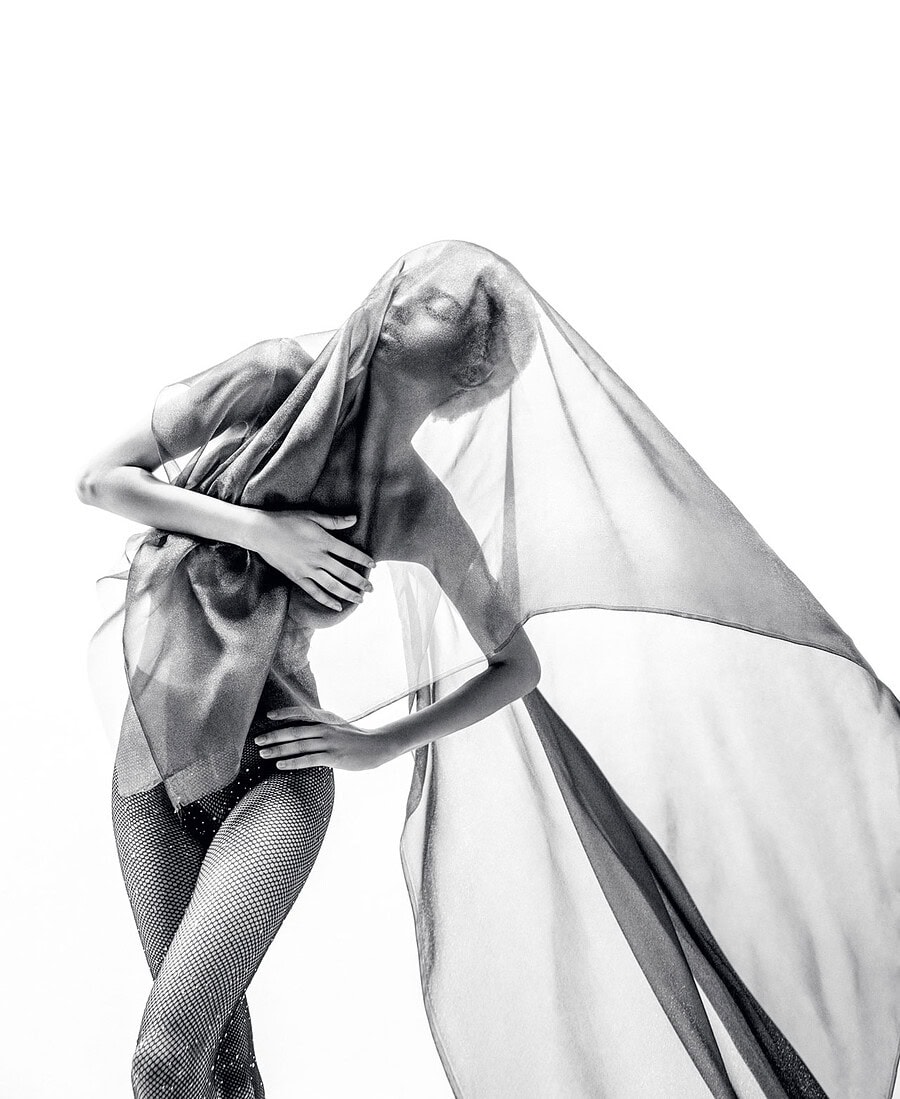 Dancer leaning sideways as translucent fabric extends through the frame