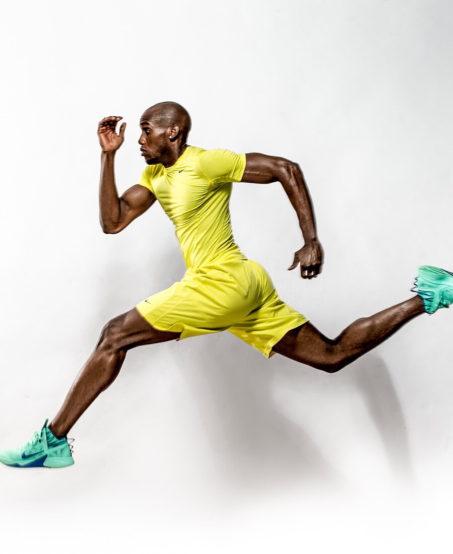Athletic male model airborne in a running pose wearing yellow sportswear and mint-green sneakers.