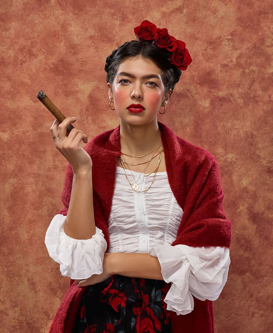Woman with red roses in her hair wearing a red shawl and white ruffled blouse while holding a cigar.