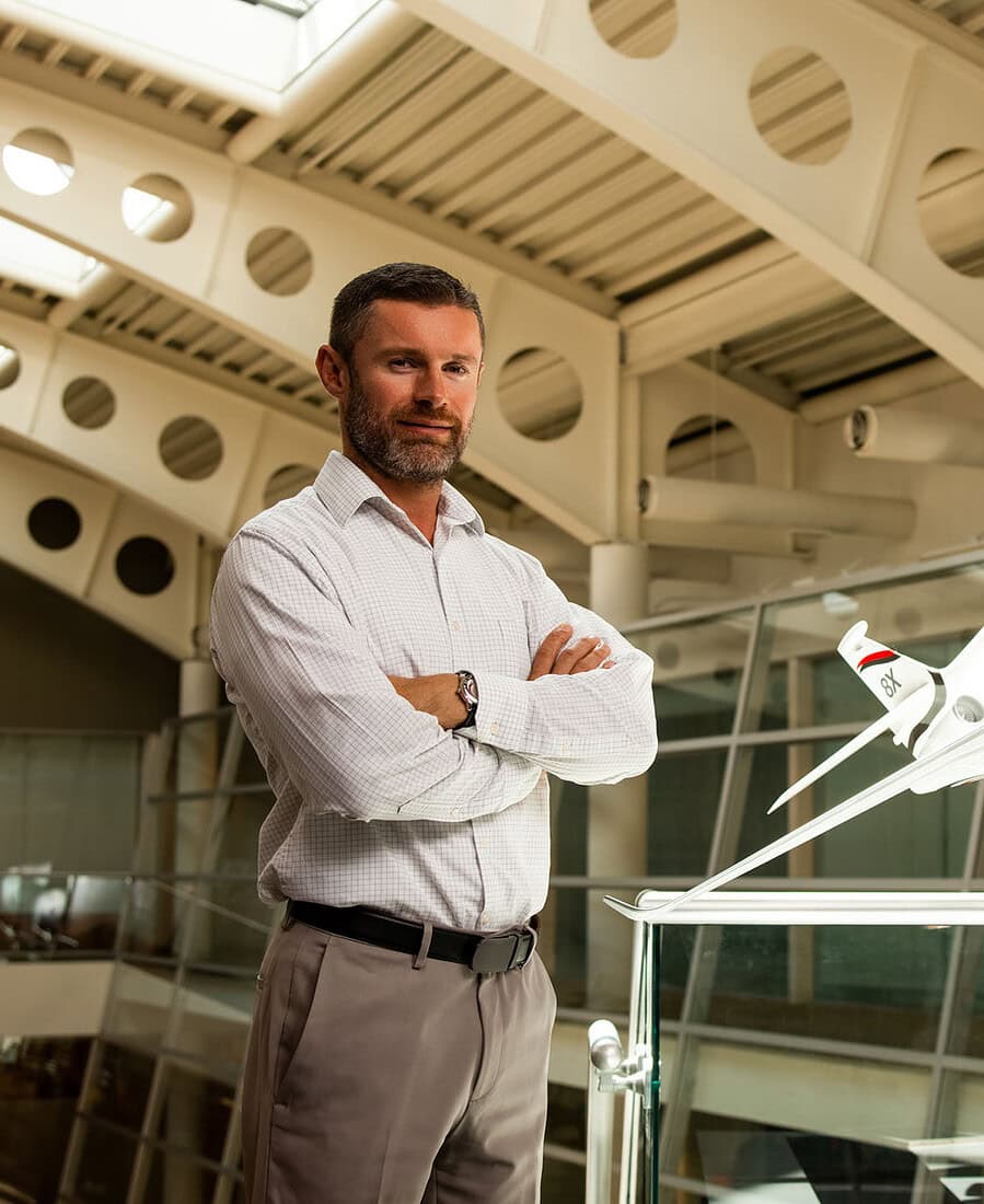 Aerospace professional standing beside a scale business jet in a modern corporate atrium.