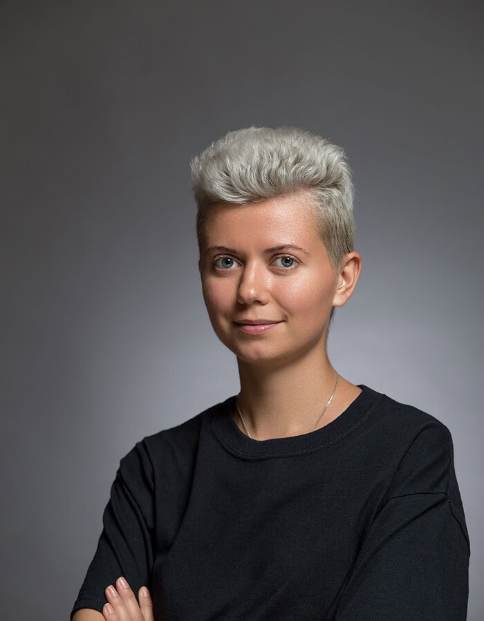 Contemporary studio portrait of a person with short silver hair wearing a black shirt.