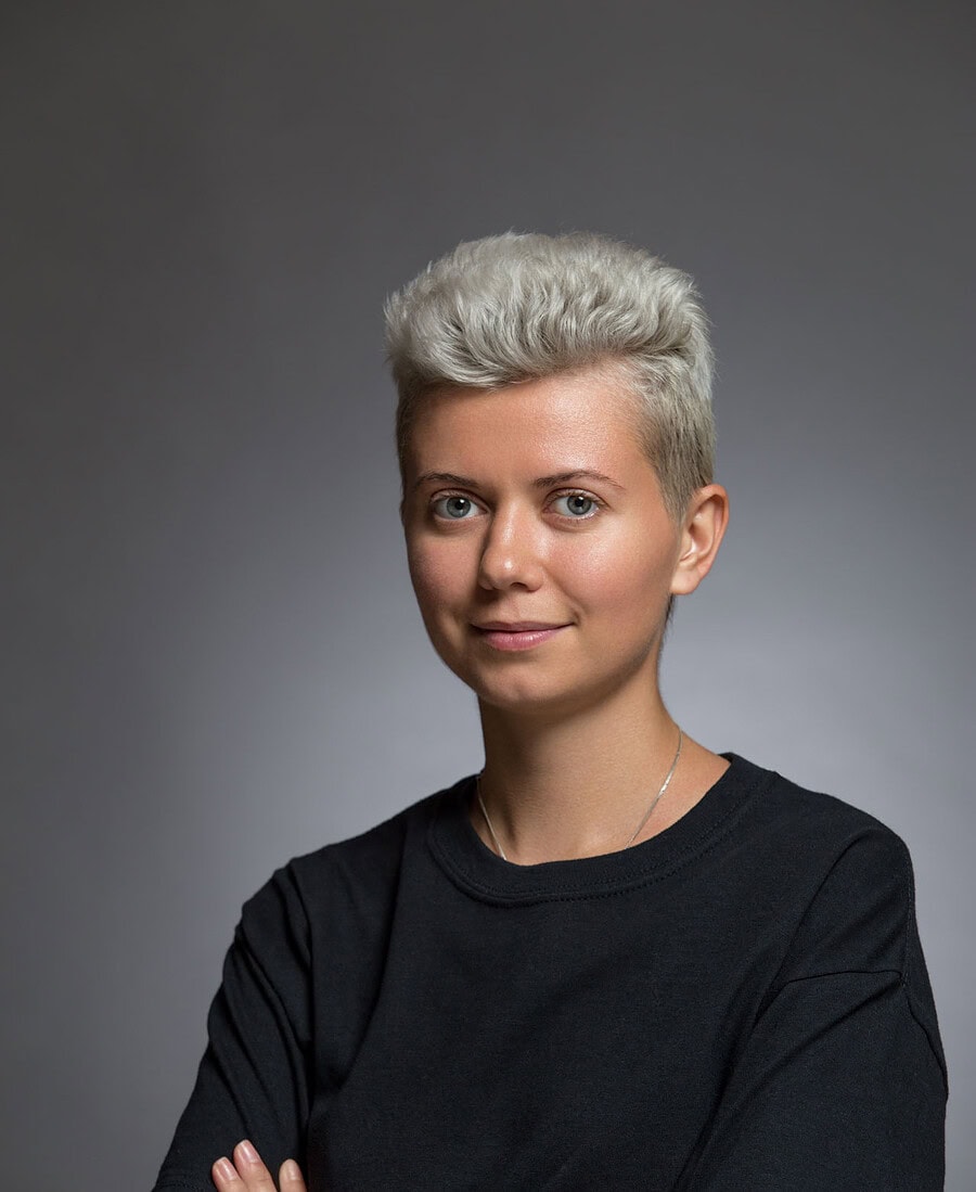 Contemporary studio portrait of a person with short silver hair wearing a black shirt.