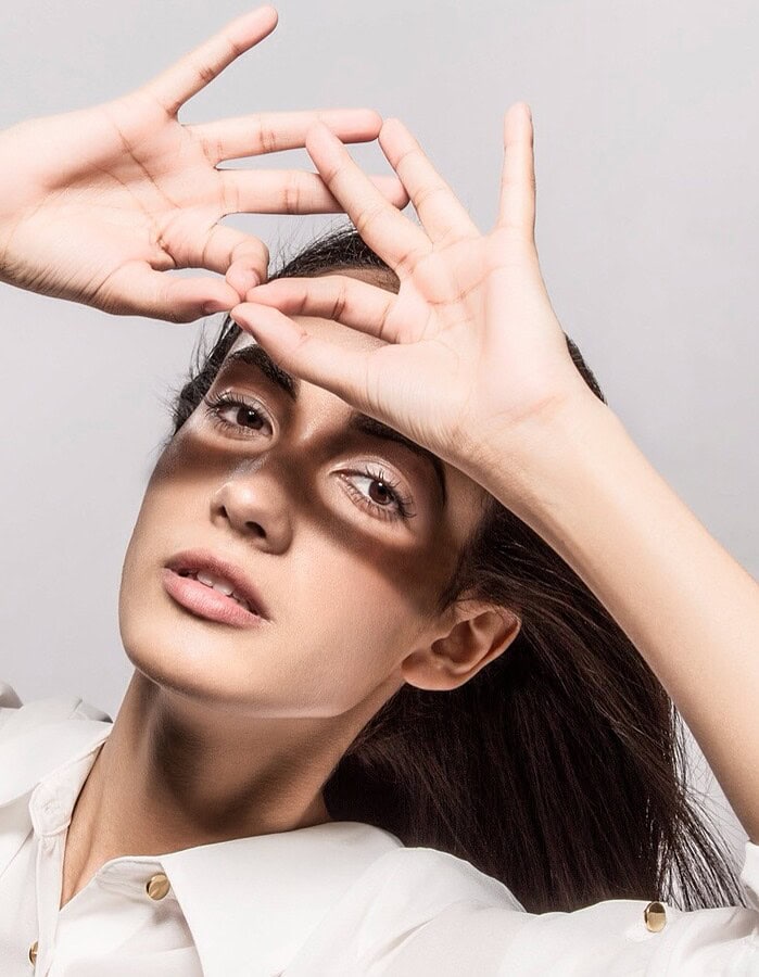 Woman with natural makeup holding both hands above her brow, casting shadows across her face