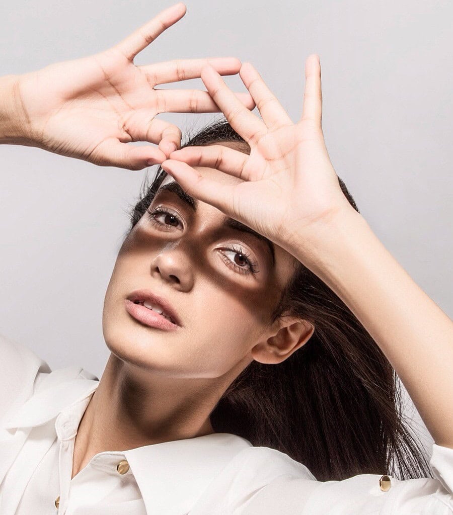 Woman with natural makeup holding both hands above her brow, casting shadows across her face