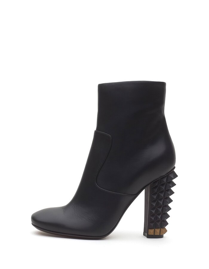 Black leather ankle boot with a sculptural studded block heel photographed on white.