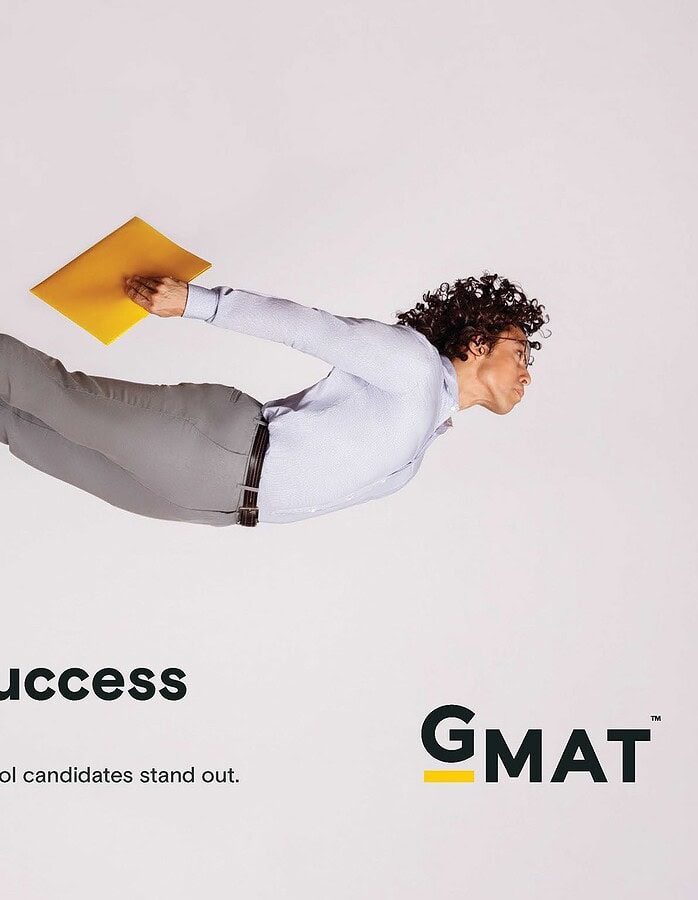 Man posed horizontally in midair while holding a yellow folder in a GMAT advertisement.