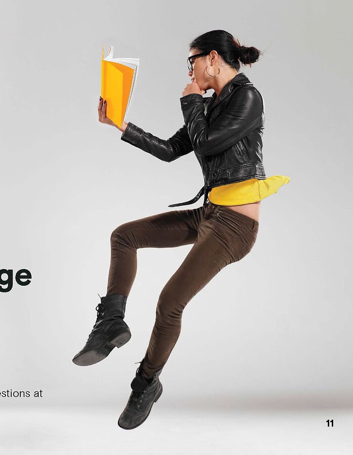 Woman in a leather jacket jumping while holding a yellow book in a GMAT campaign layout.