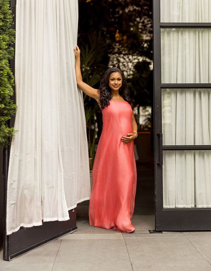 Pregnant woman in a coral gown photographed in a doorway for an editorial interview.