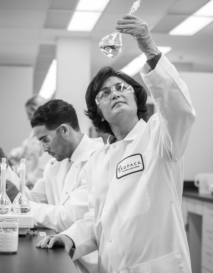 Scientist in safety glasses raising a glass flask inside a pharmaceutical laboratory.