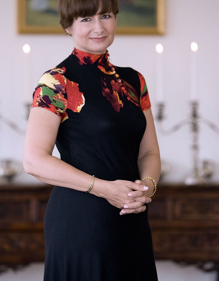 Simona-Mirela Miculescu photographed in a formal interior wearing a black dress with floral detail.
