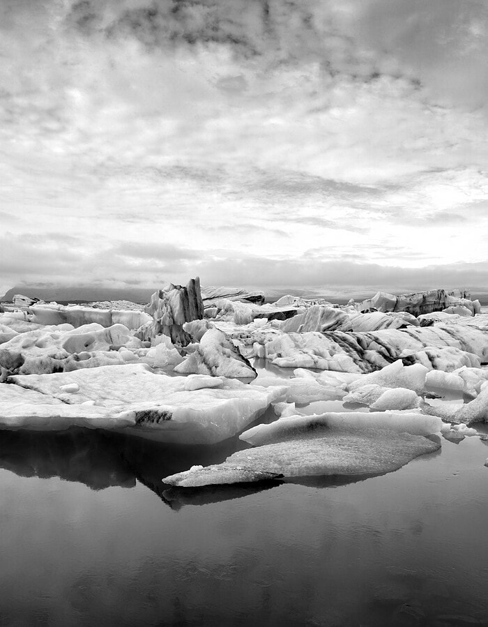 Black and white Iceland glacier lagoon with floating ice, clouds, and calm reflective water.