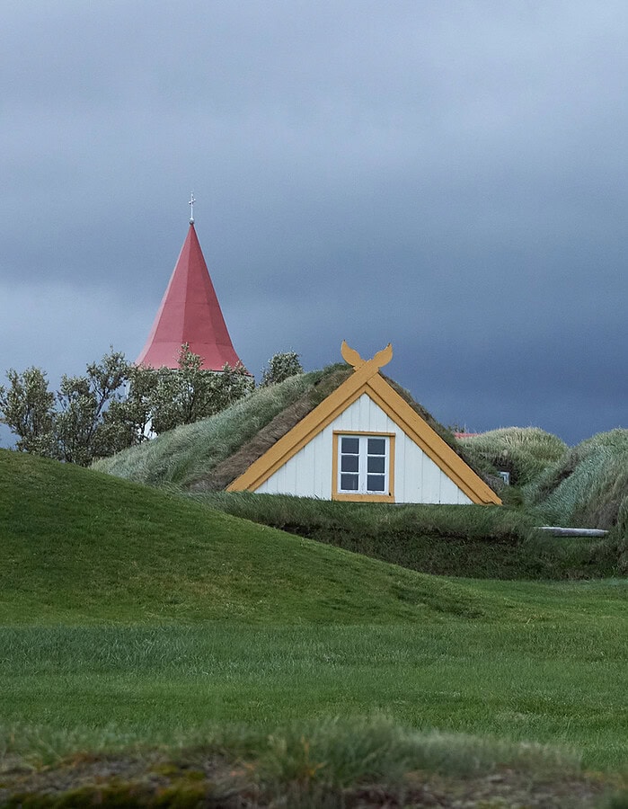 Icelandic turf-roofed buildings with yellow trim beneath a deep blue storm sky.