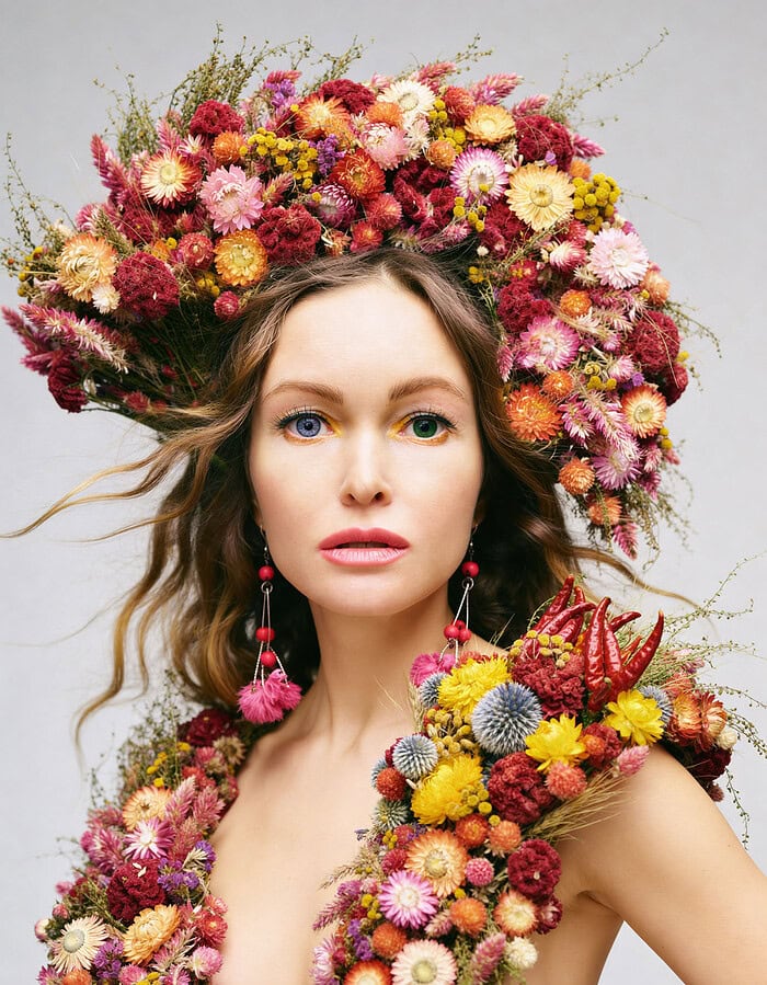 Editorial portrait of a model wearing sculptural floral styling against a clean studio background.