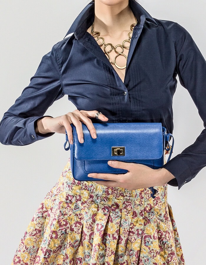 Studio fashion image of a model holding a blue clutch with a navy blouse and patterned skirt.