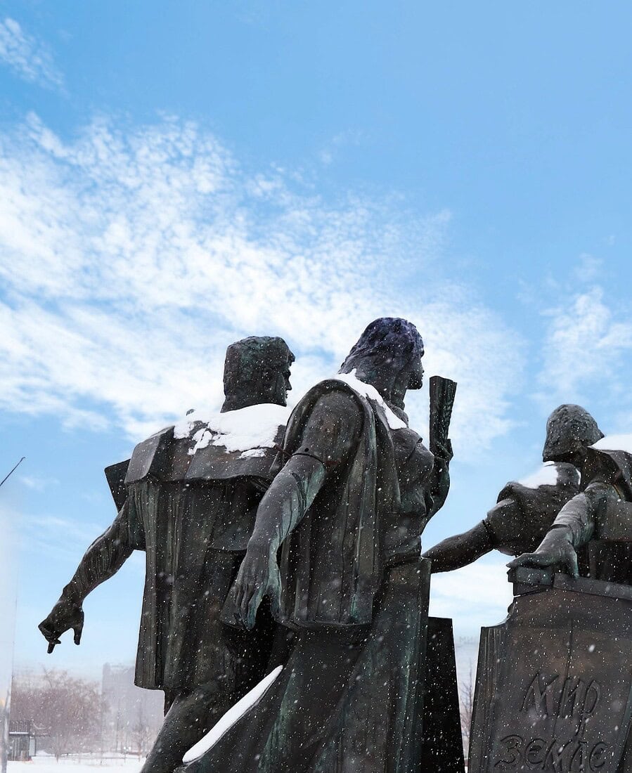 Snow-covered bronze figures of a Moscow war monument under a bright blue winter sky.