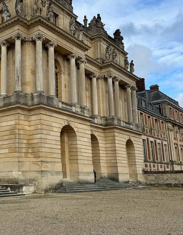 Detailed exterior view of Versailles palace architecture with columns, arches and sculpted roofline.