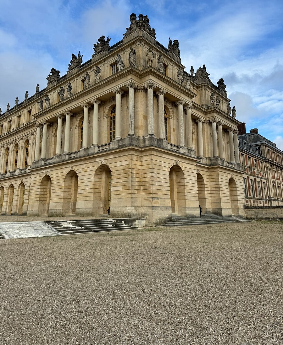 Exterior corner of the Palace of Versailles with stone columns, sculpted figures and blue sky.