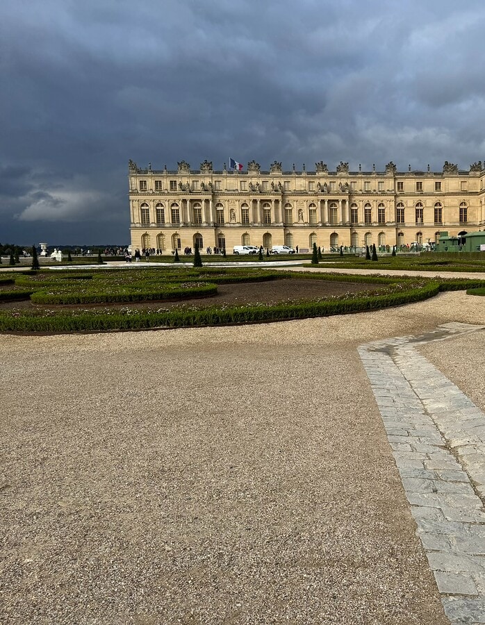 The Palace of Versailles and formal gardens under dark storm clouds in France.