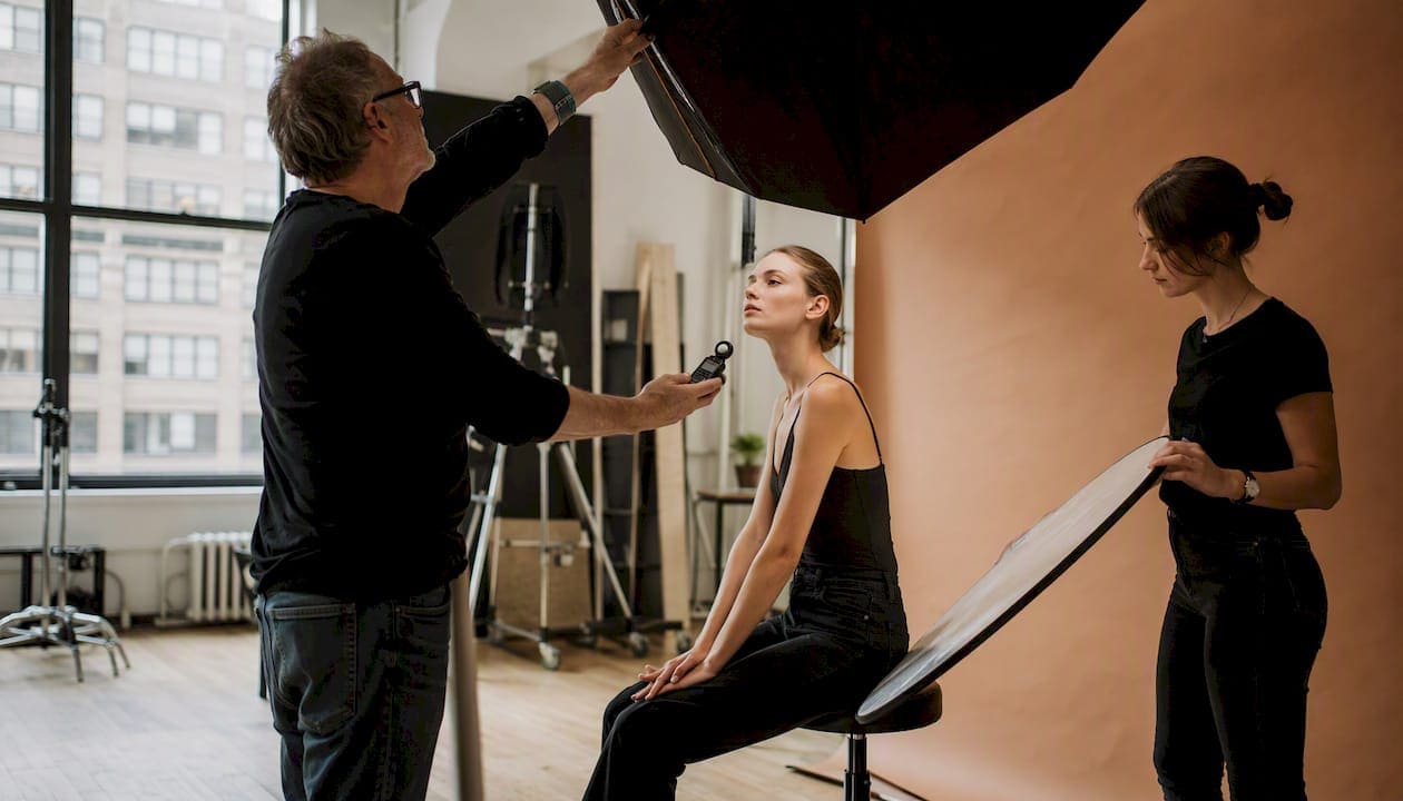 Photographer adjusting lighting with fashion model in studio