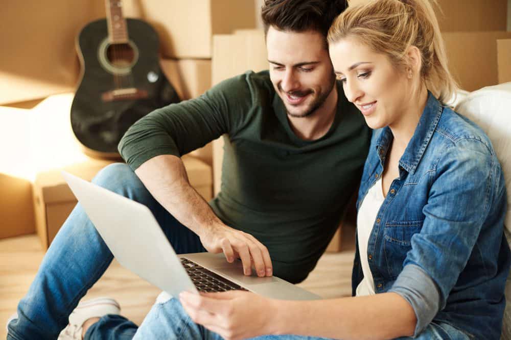 Close-up of a happy young couple using a laptop, with a guitar in the background, in a cosy home setting.