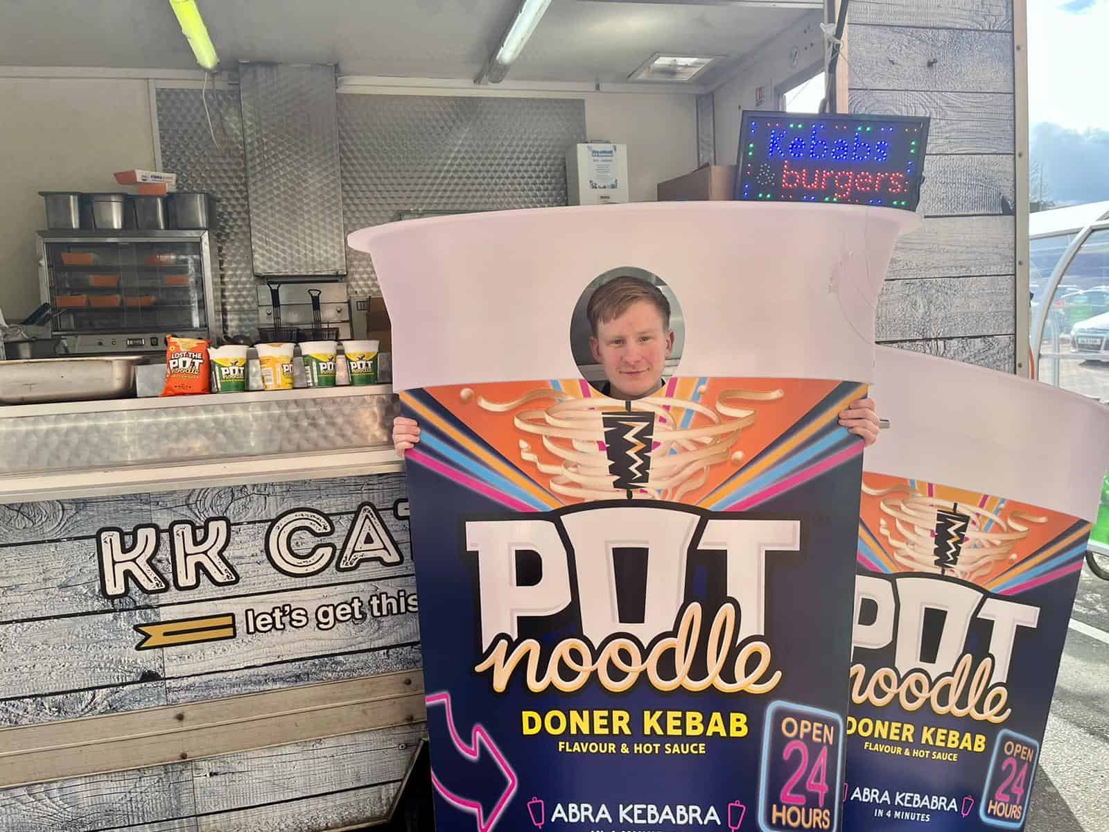 Vibrant Doner Kebab Food Stand with bright signage and person holding a colourful 'POT Noodle' sign, offering fast food and catering services.