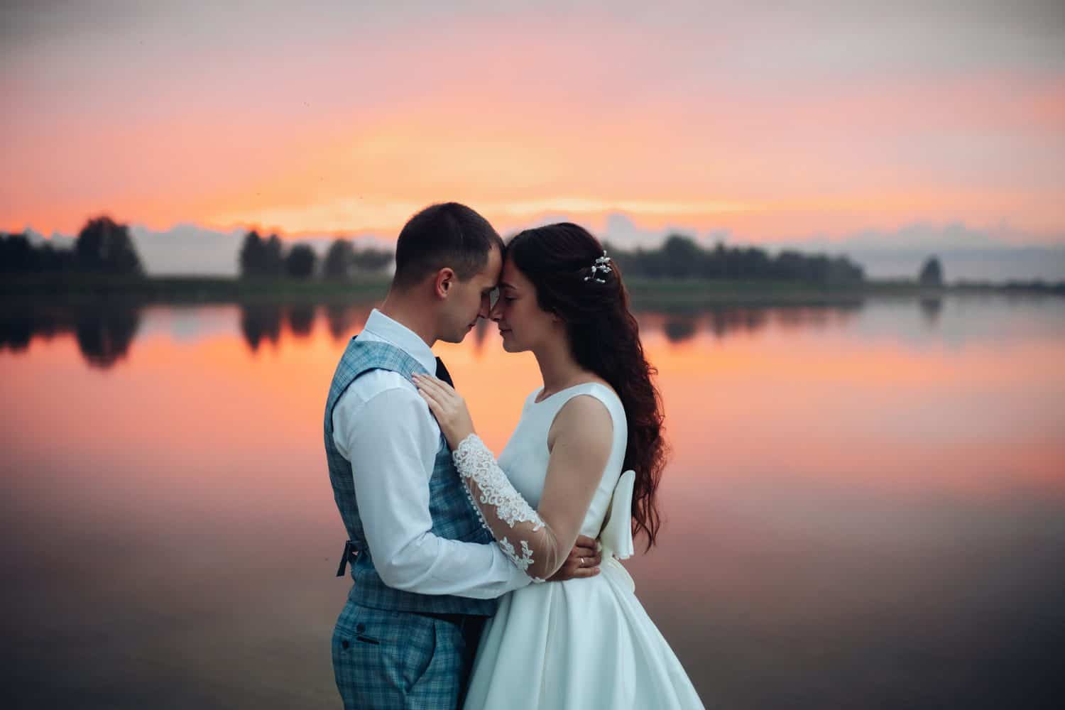 Elegant wedding couple embracing at sunset by the river.