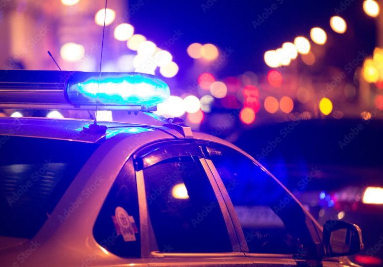 Blue light flasher atop of a police car. City lights on the background.