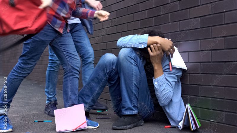 Cruel teenagers scattering classbooks of afro-american boy, school bullying