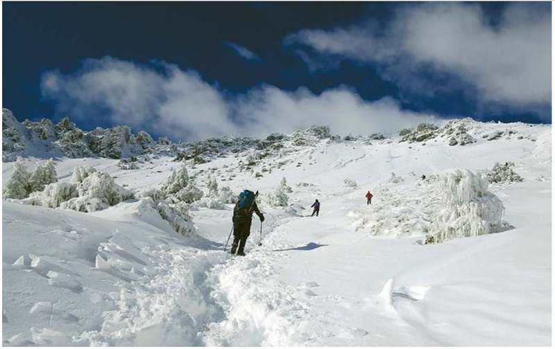Hikers climb a snow-covered mountain, navigating steep and icy terrain.