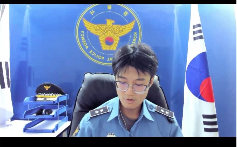 A male suspect in a Korean police scam sets up a fake police station studio for a phishing video call, wearing a high-ranking officer’s insignia.