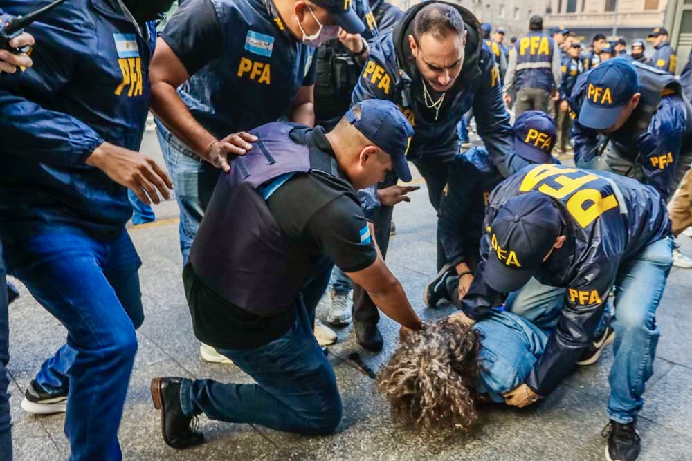 Seven police officers restrain a protester during Javier Milei’s reform protests.