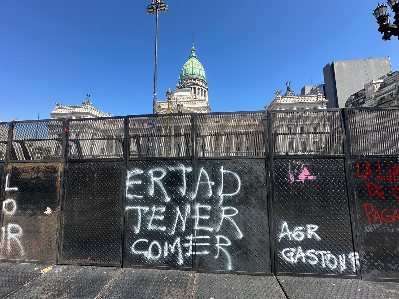 A metal barricade set up by police in Buenos Aires, covered with protest slogans.