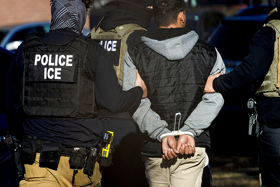 ICE agents arresting a person during an immigration raid, with officers in vests on each side