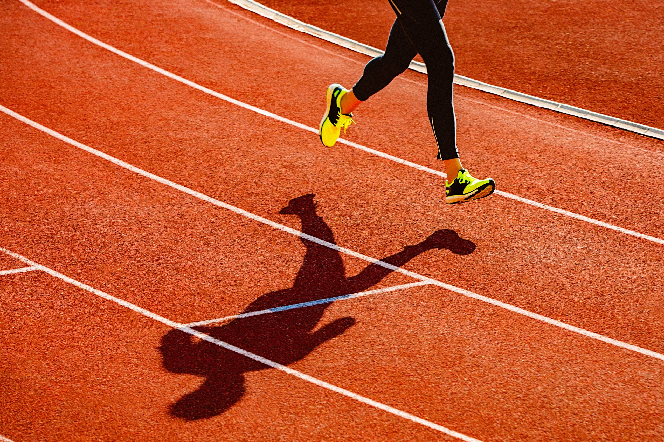 Runner's legs casting shadow on orange track during sprint, referencing transgender athlete sports debate