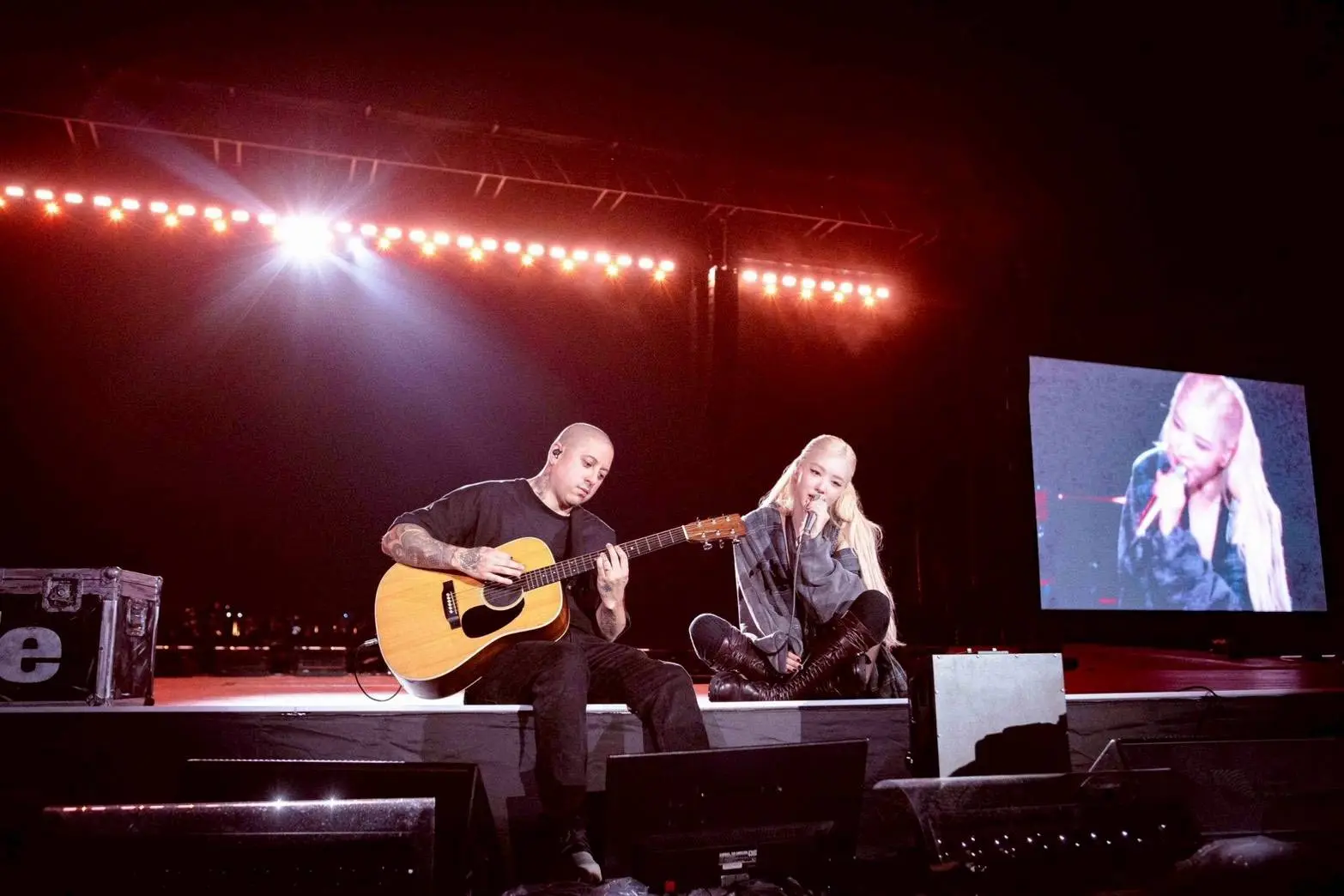 Rosé performs a late-night acoustic session with her guitarist during BLACKPINK’s tour, sitting side-by-side under soft stage lighting.