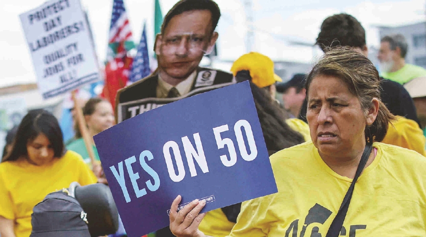 Protesters at a Los Angeles immigration rally hold signs supporting Prop 50 redistricting reform on October 4.