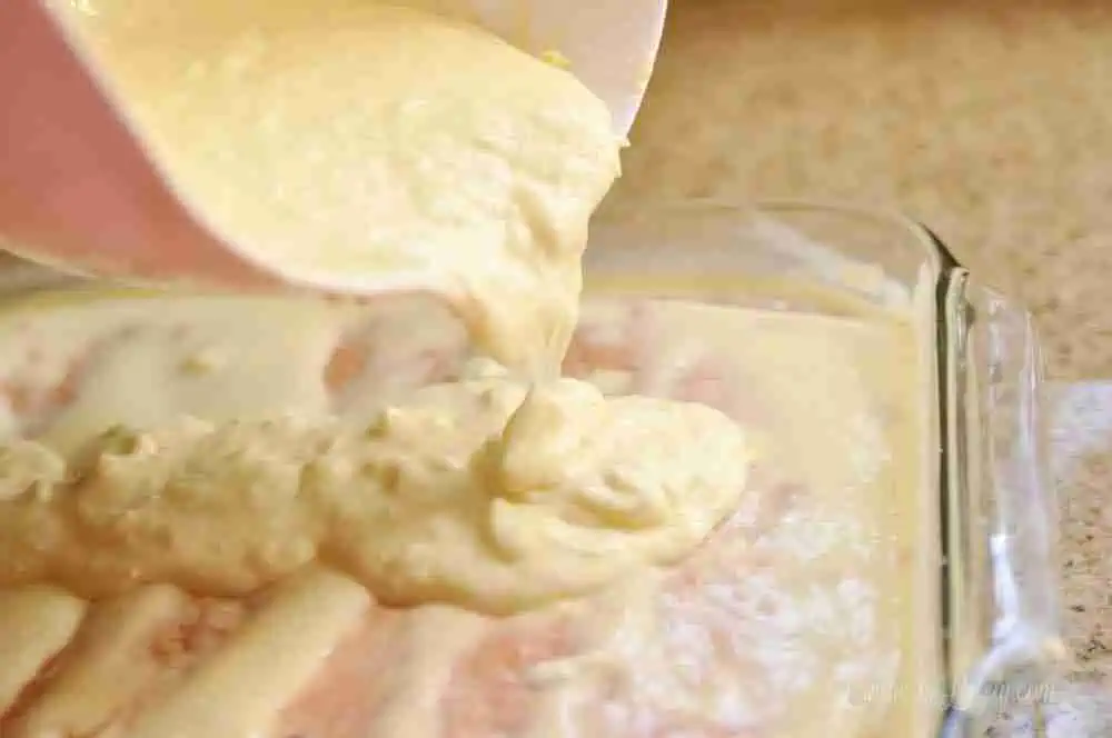 pouring pudding mix over a strawberry cake with holes.
