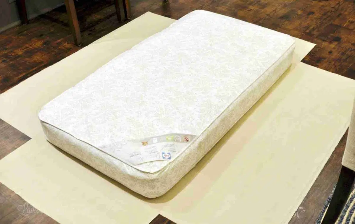 crib mattress laying on top of the start of a cover.