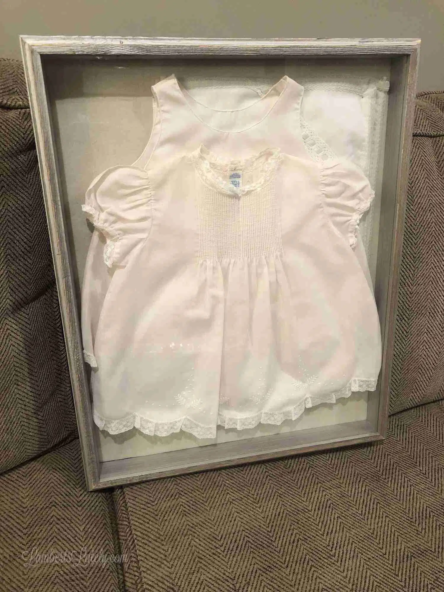 framed pink baby outfit on a couch.