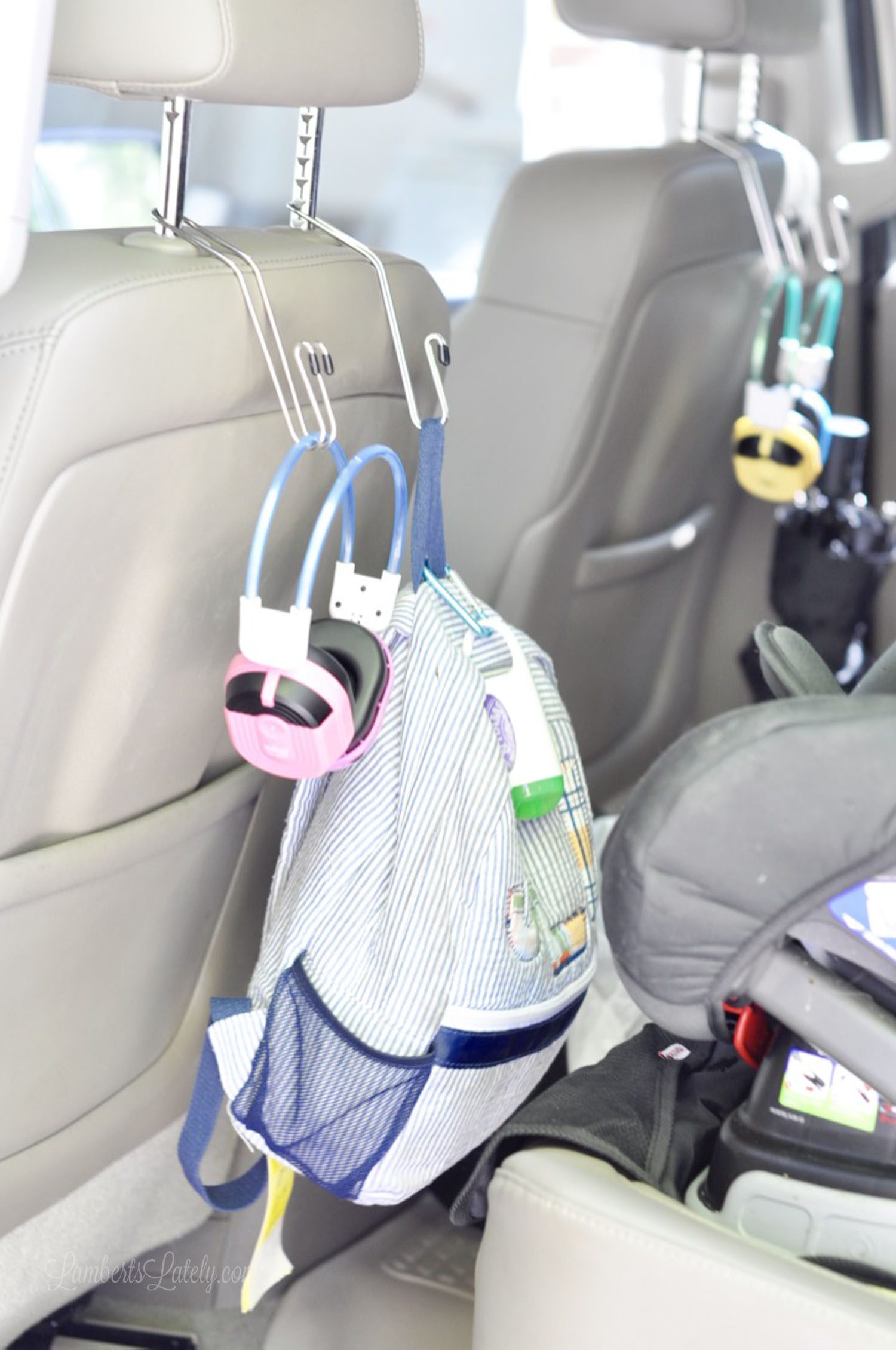 backpack and headphones hanging on the back of a car seat with metal hangers.
