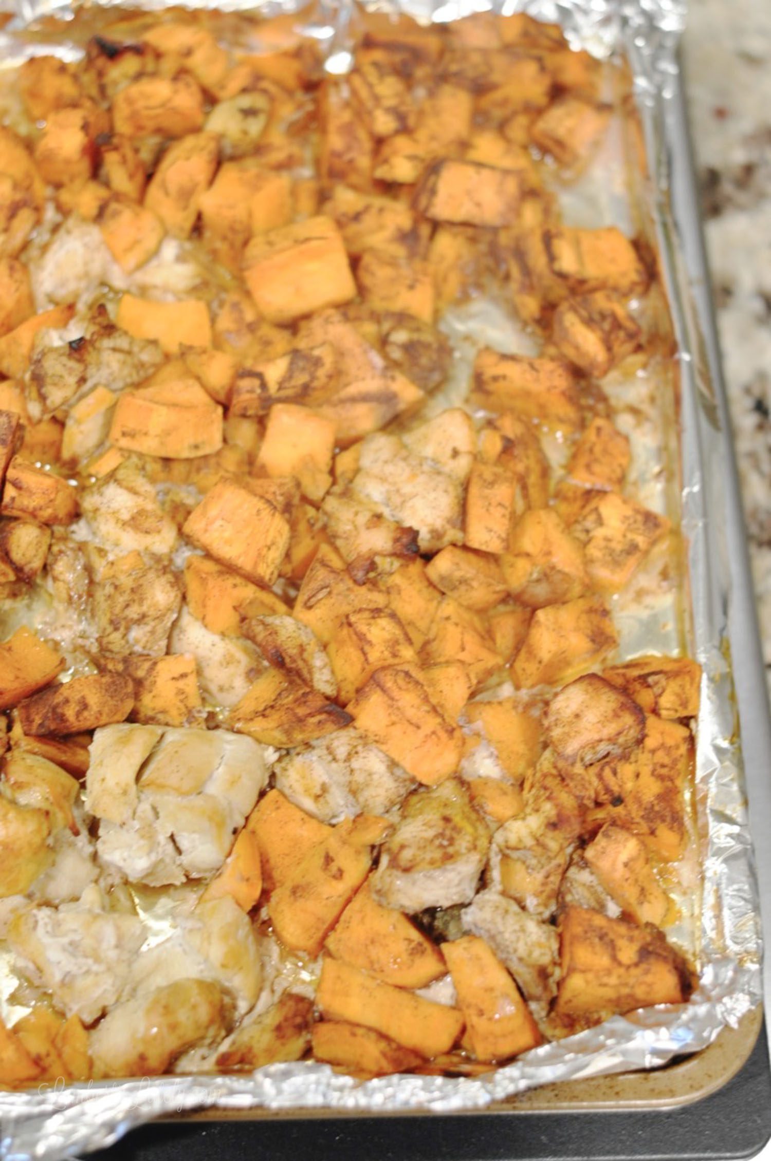 chicken and sweet potatoes on a sheet pan lined with foil.