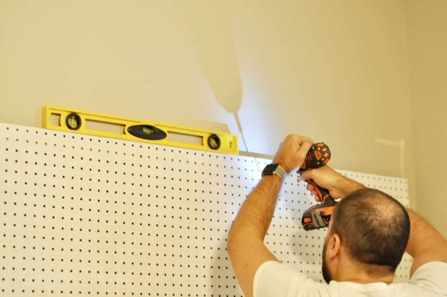 screwing pegboard into wall, with level on top.